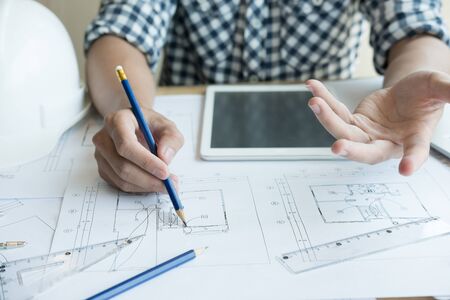 young architect working on real estate project at workplace. Male engineer hand working with living house blueprint at office. Business, people, construction and building conceptの写真素材