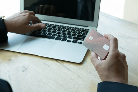 young male holding a credit card and using laptop computer for online shopping. businessman purchase goods from internet. man make payment on bank websiteの写真素材