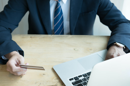 young male holding a credit card and using laptop computer for online shopping. businessman purchase goods from internet. man make payment on bank websiteの写真素材