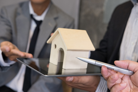 businessman showing house model on digital tablet. Realtor offer home representing by model to customer. Investment, sale and purchase propertyの写真素材