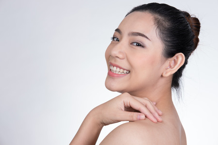Portrait of a smiling young woman with natural make-up. beautiful asian naked girl standing against white background. Skincare, healthcare, studio shot.の写真素材