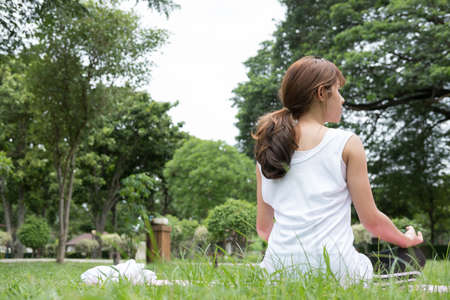 Yoga outdoors in public park in summer. Asian fitness woman sits in lotus position. Young female with zen gesturing. healthy lifestyle and relaxation conceptの写真素材