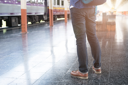 young asian man with backpack standing on platform at train station. backpacker or traveler waiting for train. journey, trip, travel conceptの写真素材