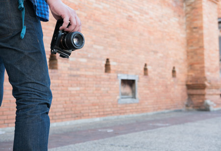 young asian man wearing blue shirt and jeans with camera and backpack standing near old orange brick...