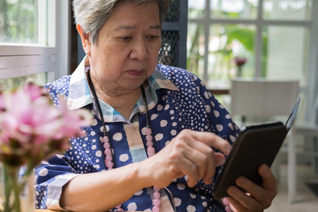 elderly senior checking social and lifestyle news with app in mobile phone. Elderly woman use smart phone for communication with people at home.の写真素材