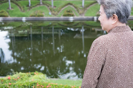 asian elder woman standing in garden. elderly senior female resting and relaxing near pond in parkの写真素材
