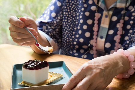 elder senoir eating blueberry cheese cake at cafe. asian elderly woman sitting and tasting delicious dessert at restaurant.の写真素材