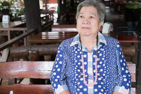 cheerful elder senoir waiting for food. happy elderly asian woman sitting at restaurant.の写真素材
