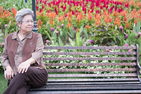 asian elder woman sitting on bench in garden. elderly senior female resting and relaxing in parkの写真素材
