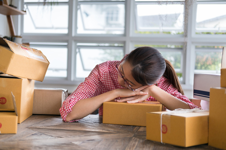 young start up small business owner doze at workplace. freelance woman lying on parcel box at her shop.  entrepreneur SME seller fall asleep at store. sleepy, tired, overworked conceptの写真素材