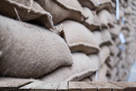 old hemp sacks containing coffee bean in warehouse. stacked sacks in storehouse with wood table for display your product.の写真素材