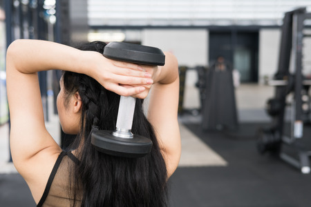 young woman execute exercise in fitness center. female athlete lift dumbbell in gym. sporty asian girl working out in health club.の写真素材
