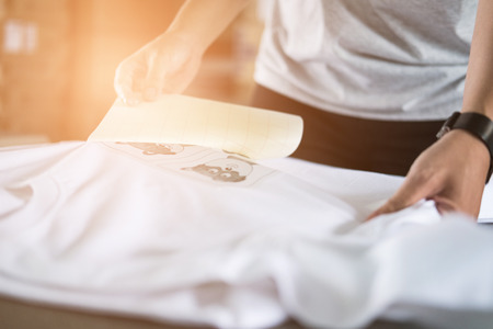 Young woman pull out paper from waterproof film on fabric. worker working on manual screen printing on t-shirt at her shop.の写真素材