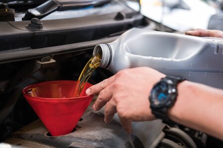 mechanic pouring oil to vehicle engine. serviceman changing motor oil in automobile repair service. maintenance and checkup in car workshop.の写真素材