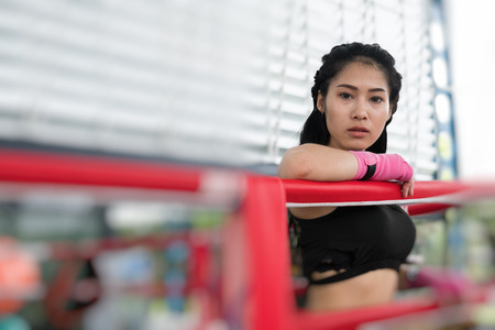 young woman prepare for exercise in fitness center. female boxer posing in boxing ring in gym. sporty asian girl resting after working out in health club. martial arts, muay thai conceptの写真素材