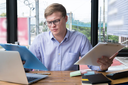 businessman use laptop with business plan document at workplace. young man with paperwork & computer at office. finance market analyst financial reportの写真素材