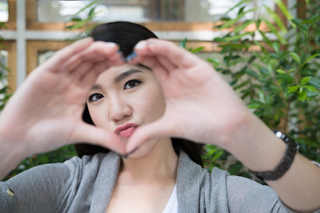 beautiful asian woman sit at outdoor cafe. young female adult with natural make-up relax at coffee shop. attractive teenager make funny face in gardenの写真素材