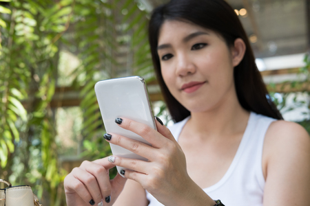 beautiful asian woman sit at outdoor cafe. young female adult use mobile phone at coffee shop. attractive teenager connect online network communication on smart phone. technology, lifestyle conceptの写真素材