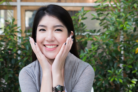 beautiful asian woman sit at outdoor cafe. young female adult with natural make-up relax at coffee shop. attractive teenager smile with happiness in gardenの写真素材