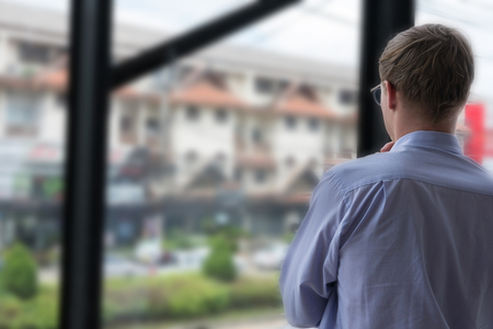 rear view of thoughtful businessman look out at the city through window at workplace. back view of young man thinking of new business project at office.の写真素材