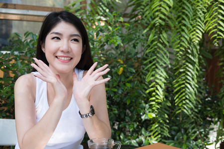beautiful asian woman sit at outdoor cafe. young female adult with natural make-up relax at coffee shop. attractive teenager smile with happiness in gardenのeditorial素材