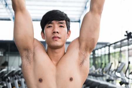 young man execute exercise with machine in fitness center. male athlete training in gym. sporty asian guy working out in health club.の写真素材