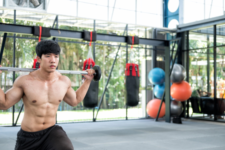 young muscular man execute exercise in fitness center. male athlete pump up muscle in gym. weightlifter working out with barbell in health club.の写真素材