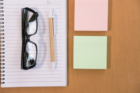 sticky note, ballpoint pen, empty notebook, eyeglasses on wood office desk. business, education concept. Top view with copy space. selective focus.の写真素材