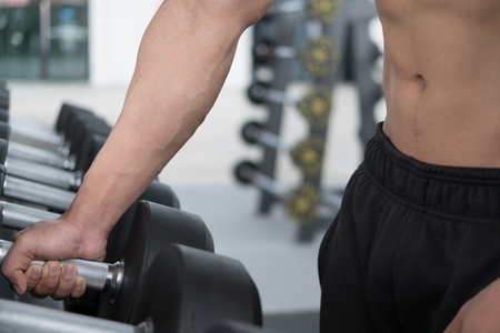 young man execute exercise in fitness center. male athlete choose dumbbell in gym. sporty asian guy working out in health club.の写真素材
