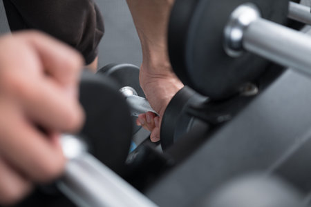young man execute exercise in fitness center. male athlete choose dumbbell in gym. sporty asian guy...