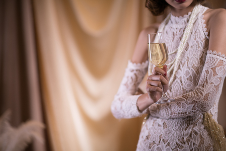 young celebrating woman in white vintage style dress. female hand hold wine glass. retro holiday celebration concept.の写真素材
