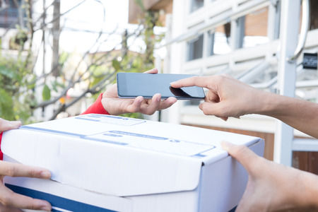 courier wearing santa claus hat delivering a parcel box to customer during christmas holiday. woman confirm delivery by signing on smart phone. online shopping, e-commerce, shipping service concept.の写真素材