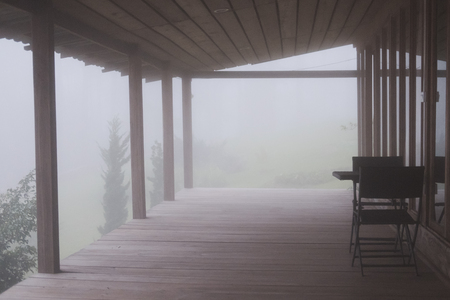wood balcony in mist and fog. terrace in cold autumn evening. chair in mysterious forest.の写真素材