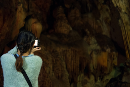young woman take photo of stone cave. tourist take picture of cavern with stalactite.の写真素材