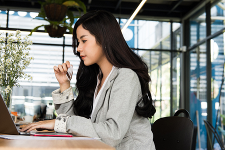 young woman holding a credit card and using laptop computer for online shopping at cafe. businesswoman purchase goods from internet at office. female adult make payment on bank website at workplaceの写真素材