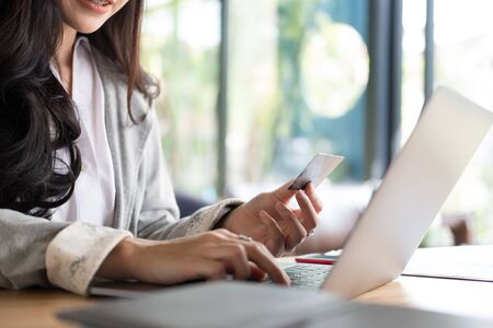 young woman holding a credit card and using laptop computer for online shopping at cafe. businesswoman purchase goods from internet at office. female adult make payment on bank website at workplaceの写真素材