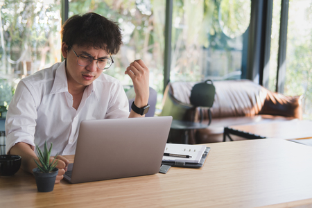 asian student using computer for learning leasson online at cafe. angry startup man working with laptop at office.  young annoyed male entrepreneur analyze data at workplace. business, education conceptの写真素材