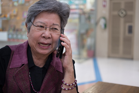 elder woman talk on mobile phone in department store. elderly female speaking on smartphone in shopping mall. asian senior have phone conversationの写真素材