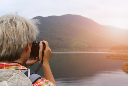 traveler man with backpack travel at mountain & lake. tourist backpacker use camera to take photo. lifestyle & summer vacation conceptの写真素材