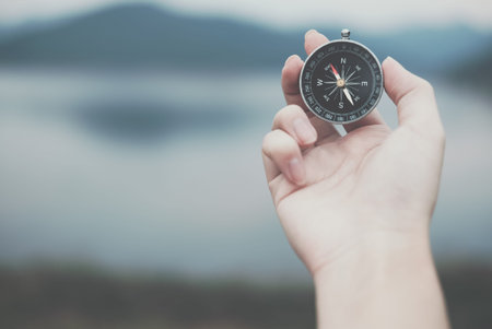 hand holding compass for searching direction outdoor. man seeking way with nature background. travel lifestyle & summer vacation conceptの写真素材