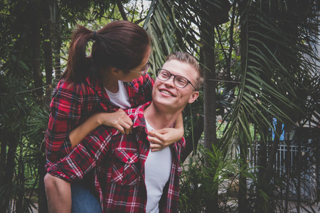 young couple in love dating in park. boyfriend piggybacking his girlfriend in valentine's day. man carry woman on his back outdoor. relationship, lover lifestyle conceptの写真素材