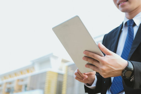 confident businessman in suit holding touchpad while standing outside building. young asian man...