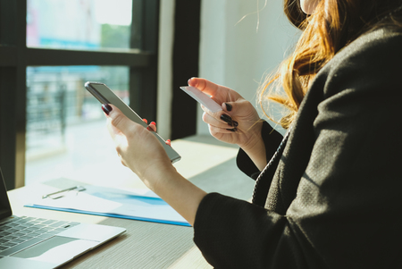 young woman holding a credit card and using smart phone for online shopping at cafe. businesswoman purchase goods from internet at office. female adult make payment on bank website at workplaceの写真素材