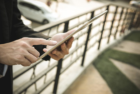 confident businessman in suit holding touchpad while standing outside building. young asian man using digital tablet for work outdoorsの写真素材
