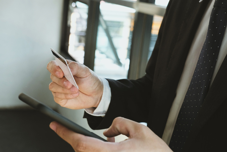 young man holding a credit card and using smart phone for online shopping at cafe. businessman purchase goods from internet at office. male adult make payment on bank website at workplaceの写真素材