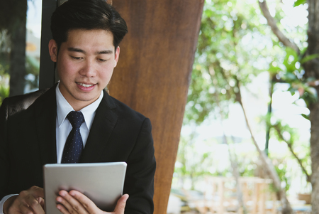 confident businessman in suit holding touchpad while standing outside building. young asian man using digital tablet for work outdoorsの写真素材