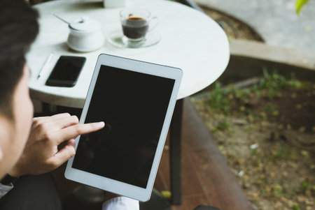 confident businessman in suit holding touchpad while sitting at cafe. young asian startup man using digital tablet for work at coffee shopの写真素材