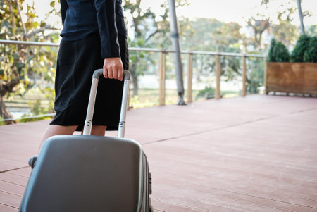 businesswoman pulling luggage outdoors. woman carrying baggage for business trip. asian female holding trolley case outside building.の写真素材