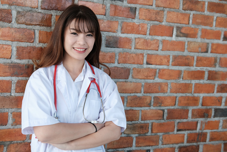Confident smiling young female doctor posing with arms crossed.  Portrait of asian medical staff, physician or practitioner on white backgroundの写真素材