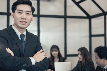 asian businessman smiling at camera while colleagues have meeting at office. business people working with co worker team at workplaceの写真素材